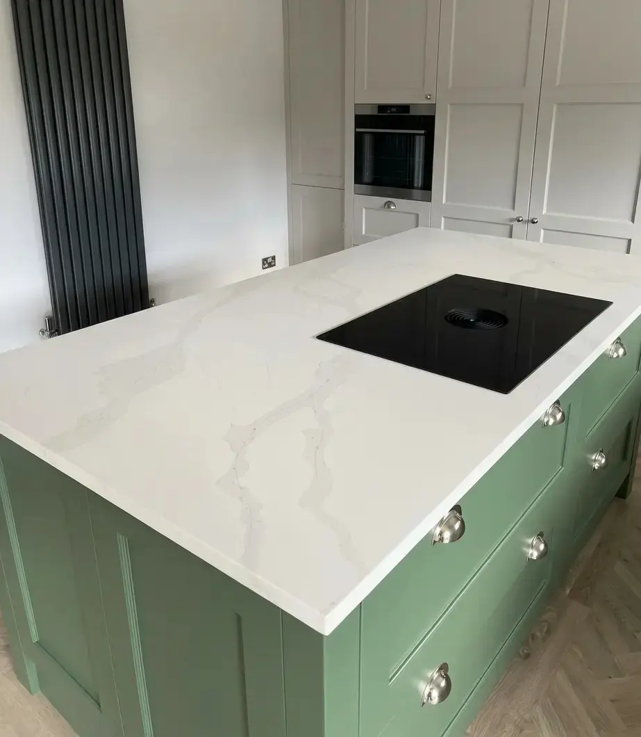 White quartz kitchen island with green cabinets and flush-fit induction hob